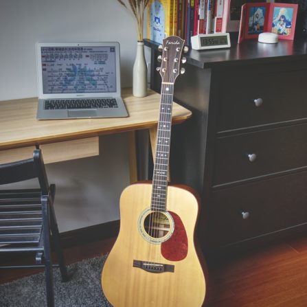 brown acoustic guitar beside black wooden drawer